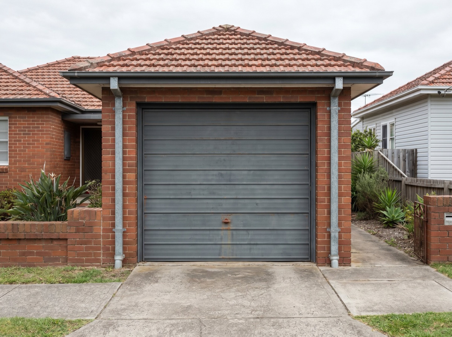 An older single-panel tilt garage door on a Newcastle brick-and-tile home